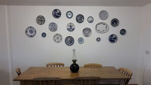 Un comedor con mesa y sillas de madera, un jarrón decorativo y una pared con platos azules y blancos.