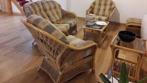 Una sala de estar con muebles de mimbre, una mesa de centro de vidrio y una pila de libros.