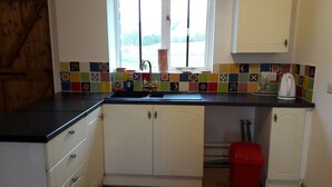 Una cocina con armarios blancos, encimera negra, salpicadero de azulejos coloridos, una ventana y un cubo de basura rojo.