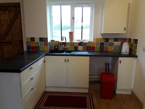 A kitchen with white cabinets, a black countertop, a colorful tile backsplash, a window, and a red trash bin.