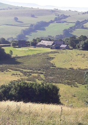A rural landscape with rolling hills, a barn, and a small cluster of houses.