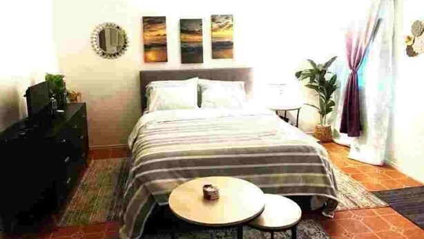 Een slaapkamer met een bed, nachtkastjes, een dressoir en een raam met gordijnen.