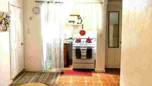Een smalle gang met een keuken aan het einde, inclusief een fornuis, een spoelbak en een raam met gordijnen.