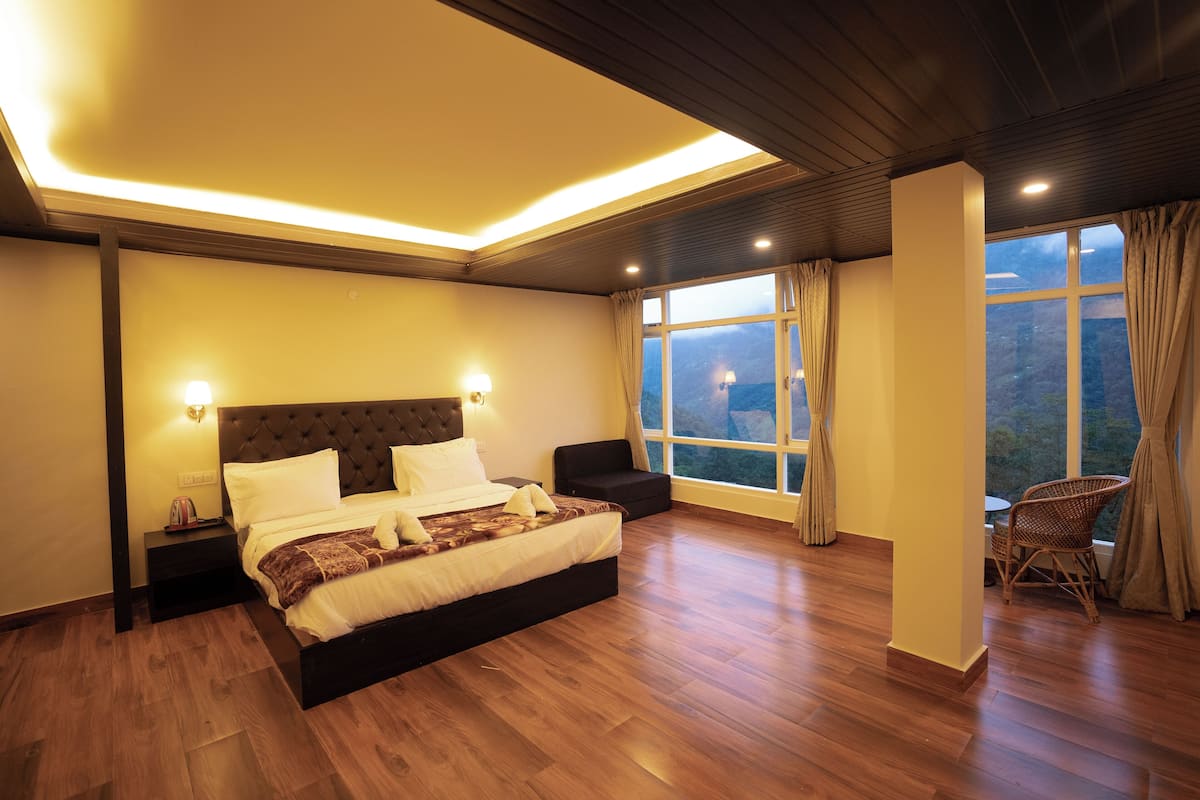 A modern bedroom with a large bed, bedside tables, a chair, and a view of the outdoors through a window.