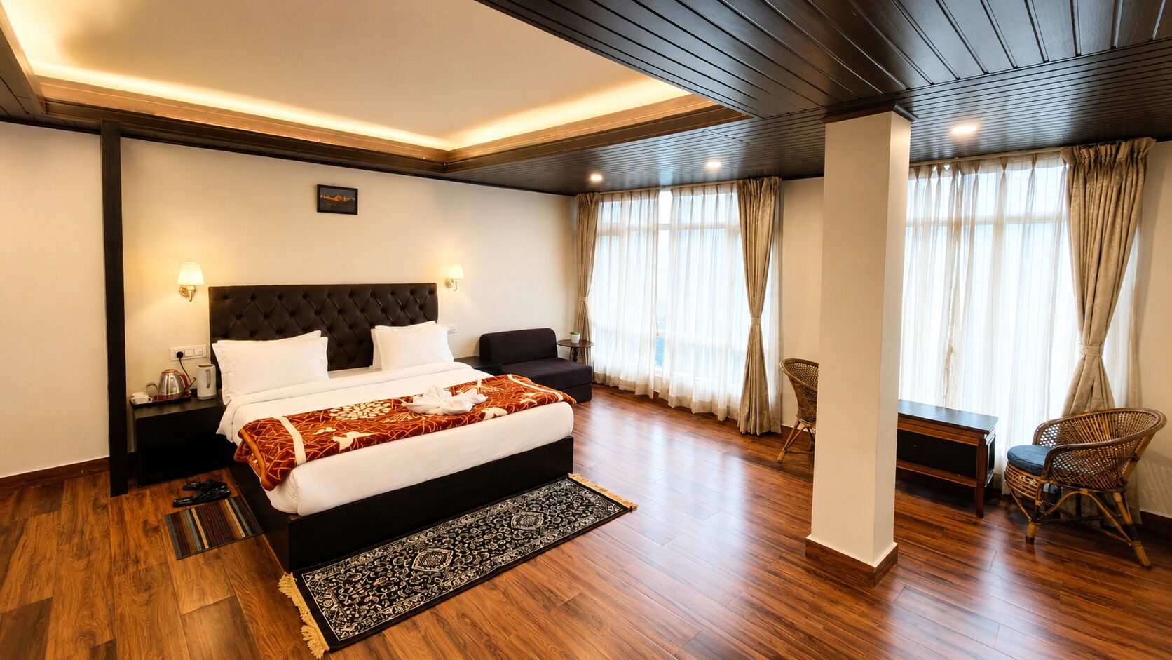 Ein Hotelzimmer mit einem großen Bett, einem Nachttisch, einem Sessel, einem kleinen Tisch und einem Fenster mit Vorhängen.