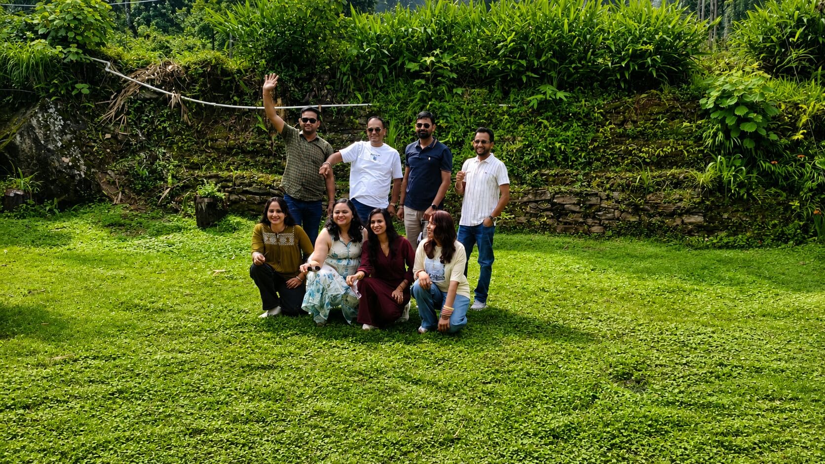 A group of people posing in a grassy outdoor area with dense foliage in the background.