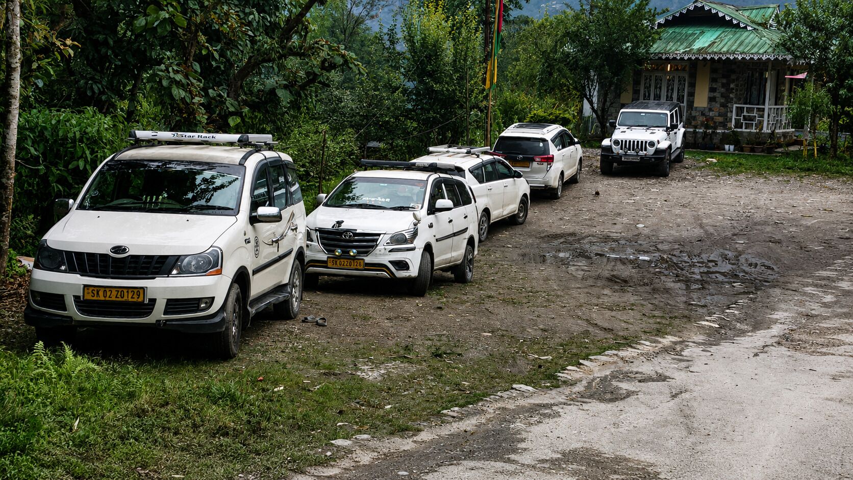 A row of white vehicles parked on a dirt road with a house in the background.