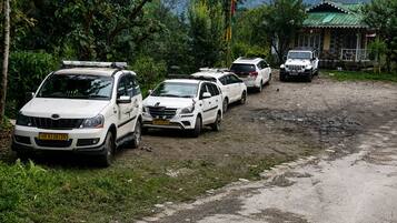 A row of white vehicles parked on a dirt road with a house in the background.