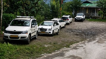 A row of white vehicles parked on a dirt road with a house in the background.