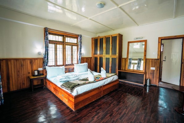 A wooden-framed bed with a window, a wardrobe, and a mirror in a room with wooden flooring and walls.