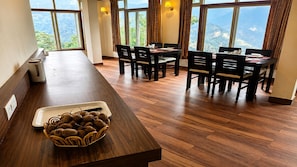 Un comedor con una larga mesa de madera y sillas, una mesa de buffet con un plato de comida, y grandes ventanales que ofrecen vistas al exterior.