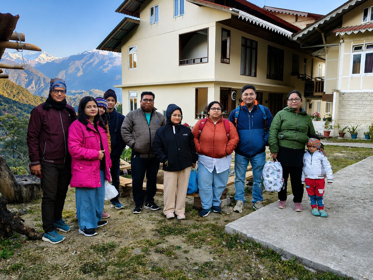 A group of people standing in front of a two-story building with a mountainous backdrop.
