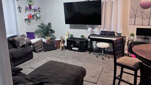 A living room with a flat-screen TV, a piano, a couch, and a coffee table. - Comfortable 2-bedroom house in Boise. Hot Tub. Fenced yard. Pet friendly. (Boise)