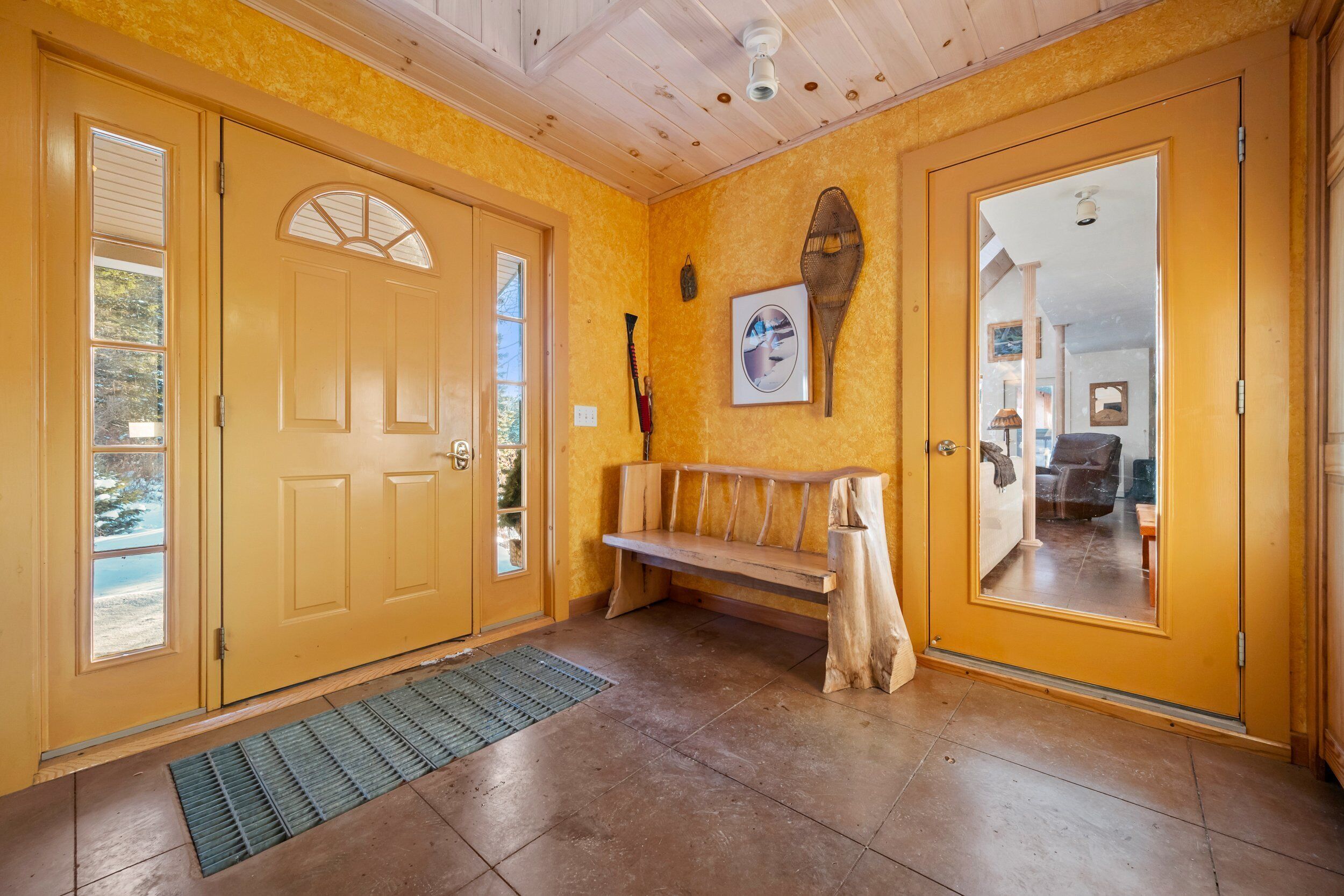 A hallway with yellow walls, a wooden bench, and a door with a mirror.