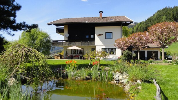 Ein zweistöckiges Haus mit Garten, Teich und Bergblick.