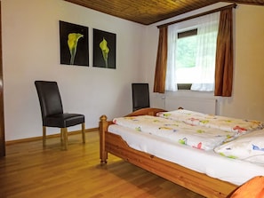 A bedroom with a wooden bed, two black chairs, a window with curtains, and two wall-mounted paintings. - Cosmea in Millstatt by Interhome (Millstadt)