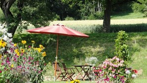 Un jardin avec un parasol rouge, des chaises en bois et une variété de fleurs.