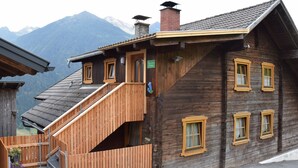 Una cabaña de madera con una escalera de madera que lleva a la entrada, una chimenea y ventanas con marcos de madera.