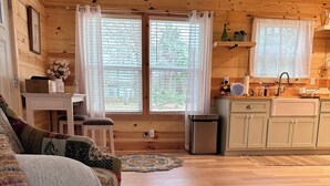 Un acogedor interior de cabaña con suelo de madera, un sofá, una mesa de comedor y una zona de cocina con armarios y un lavabo.