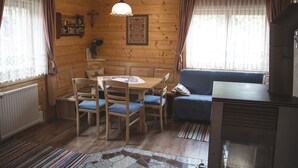 A cozy cabin interior with a wooden dining table, blue cushioned chairs, a blue sofa, and a small television. - Holzhaus Klippitzblickhütte by Interhome (Bad St. Leonhard im Lavanttal)