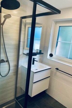 Ein modernes Badezimmer mit einer gläsernen Duschkabine, einem weißen Waschbecken und einem Fenster für natürliches Licht.