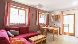A cozy living room with a red sofa, wooden dining table, and a cross on the wall.