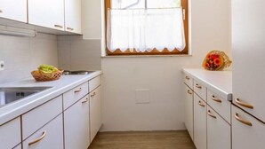 A narrow kitchen with white cabinets, a window with a white curtain, and a wooden floor.