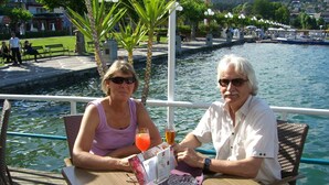Two people seated at a table with a drink and menu, overlooking a body of water with boats and a dock in the background. - Erle in Feistritz im Rosental by Interhome (Feistritz im Rosental)