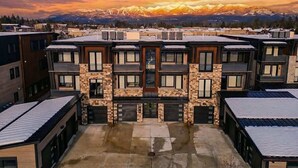 A multi-story building with a central courtyard, large windows, and a view of snow-capped mountains. - 4 Bd / 4 Bth | Luxury Condo | Hot Tub | Sleeps 10 (Whitefish)