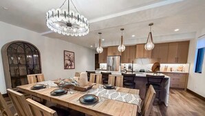 A modern kitchen with wooden cabinets, a central island, pendant lighting, and a dining area with a wooden table and chairs. - 4 Bd / 4 Bth | Luxury Condo | Hot Tub | Sleeps 10 (Whitefish)