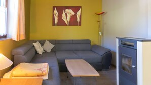 Un salon avec un canapé gris, une table en bois, un petit banc en bois, une lampe sur pied et un poêle moderne.