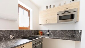 Ett modernt kök med en svart spishäll, inbyggd ugn och mikrovågsugn. Det finns ett fönster med träram och en bänkskiva med ett stänkskydd som liknar marmor.