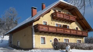A two-story chalet with a wooden balcony, a sloped roof, and a snow-covered ground. - Typ 1 im Haus Huber in Bleiburg by Interhome (Bleiburg)