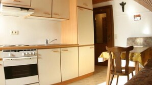 A kitchen with wooden cabinets, a stove, and a dining area with a table and chairs. - Typ 3 im Haus Huber in Bleiburg by Interhome (Bleiburg)