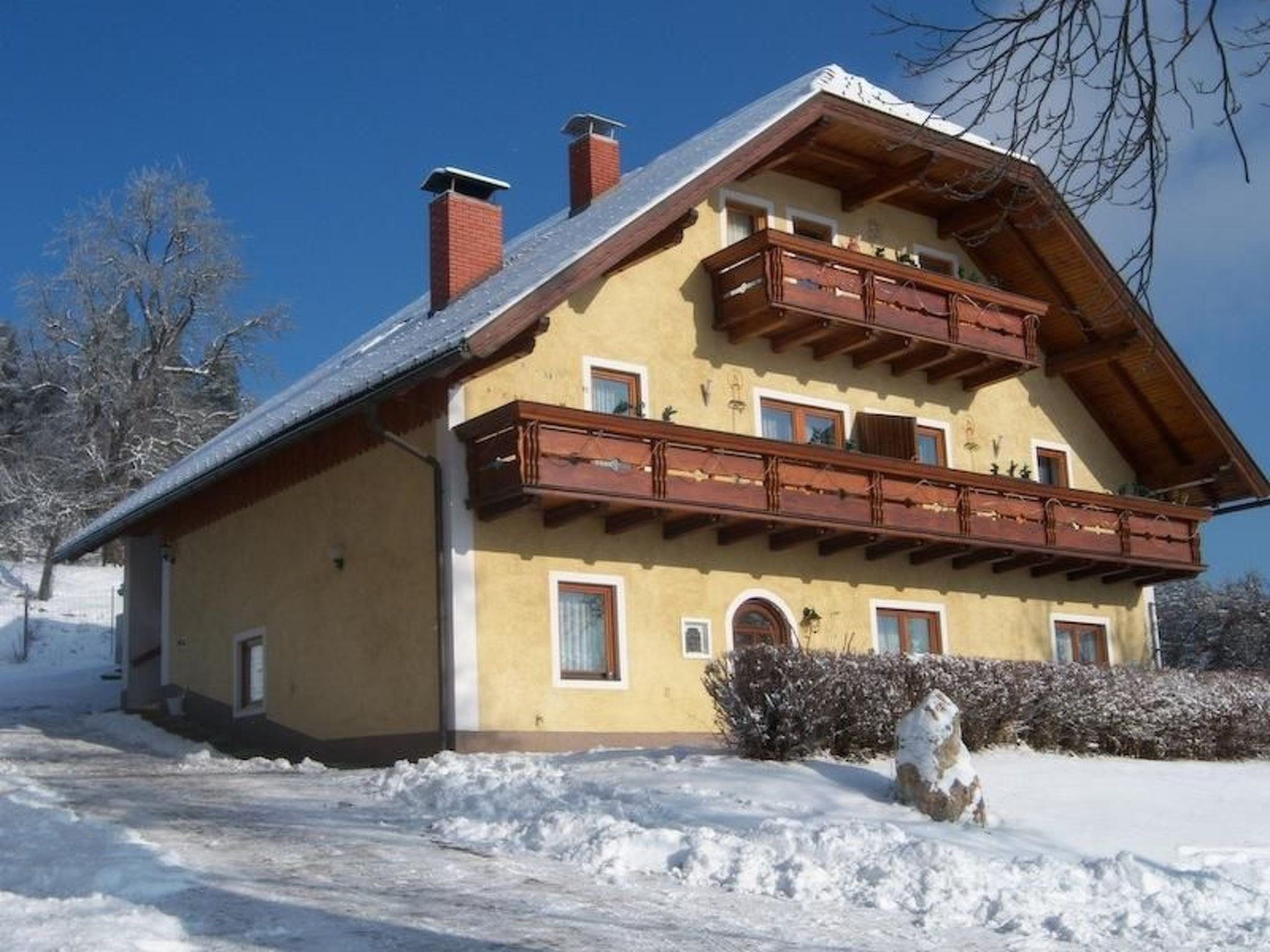 Un chalet de dos pisos con un balcón de madera, techo inclinado y suelo cubierto de nieve.