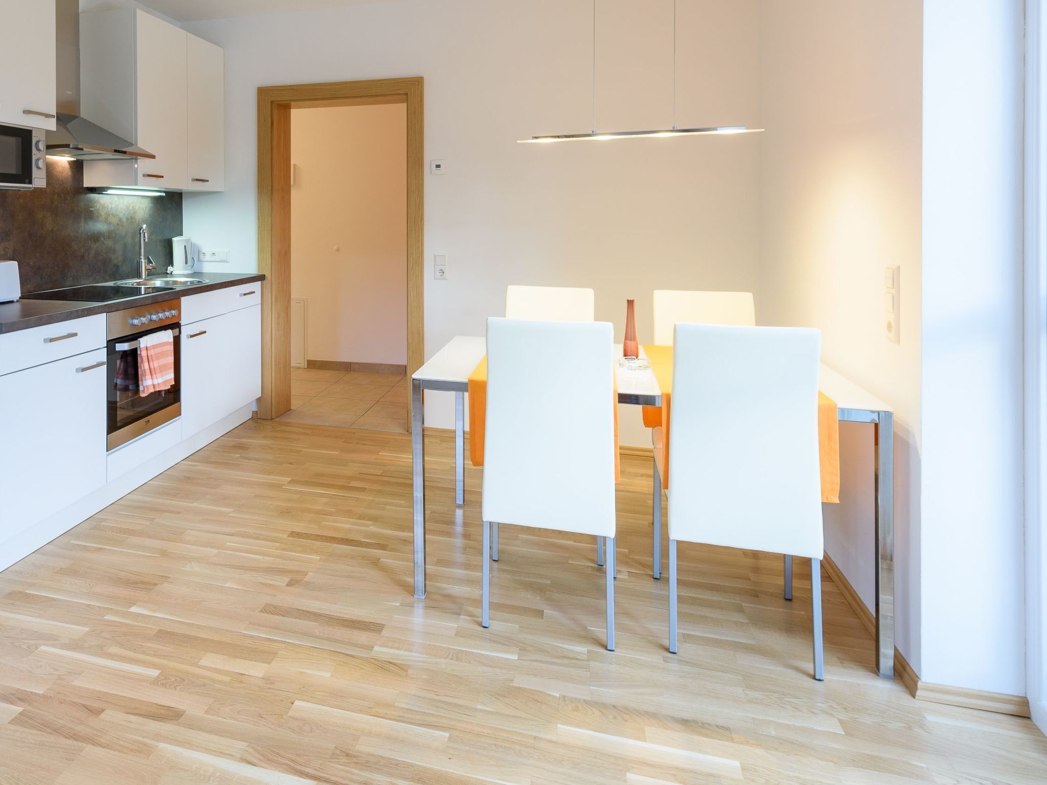 Une cuisine moderne avec des armoires blanches, un four en acier inoxydable et un plancher en bois.