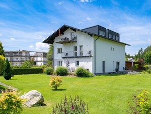 Ein modernes, zweistöckiges Wohnhaus mit Balkon, umgeben von einem gepflegten Rasen und Garten.