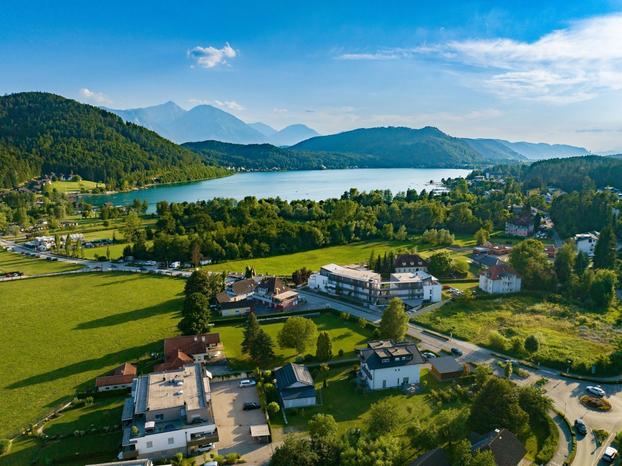 Ein Luftbild einer Stadt am Seeufer mit Wohnhäusern, einem großen See und Bergen im Hintergrund.