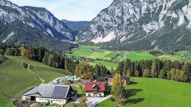 Ein ländliches Anwesen mit einem Hauptgebäude, Solaranlagen und einem großen grünen Feld.