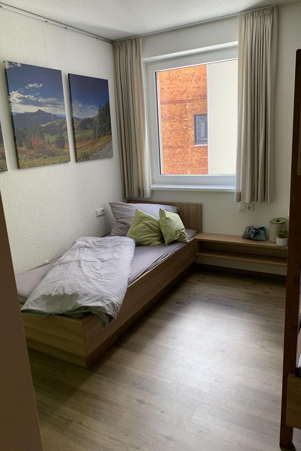 Une pièce avec un lit, une fenêtre et une vue sur un immeuble en briques.