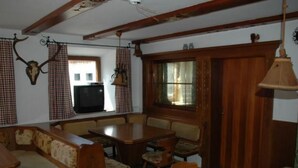 Comedor tradicional con mesa de madera y bancos, televisor y cortinas estampadas.