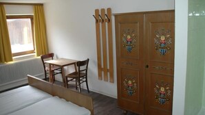 Un dormitorio con una cama, un armario de madera con paneles decorativos, una mesita con una silla y una ventana con cortinas.