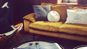 Ein gelbes Sofa mit vielen Kissen, ein schwarzer Sessel und ein Tisch mit einem offenen Buch.