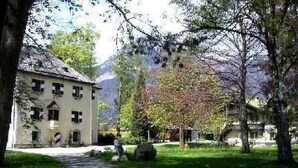 Ein Weg führt zu einem Gebäude mit einer symmetrischen Fassade, umgeben von üppiger Vegetation und Bäumen.