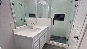 Een moderne badkamer met een douchecabine van glas, een witte wastafel en een grote spiegel.