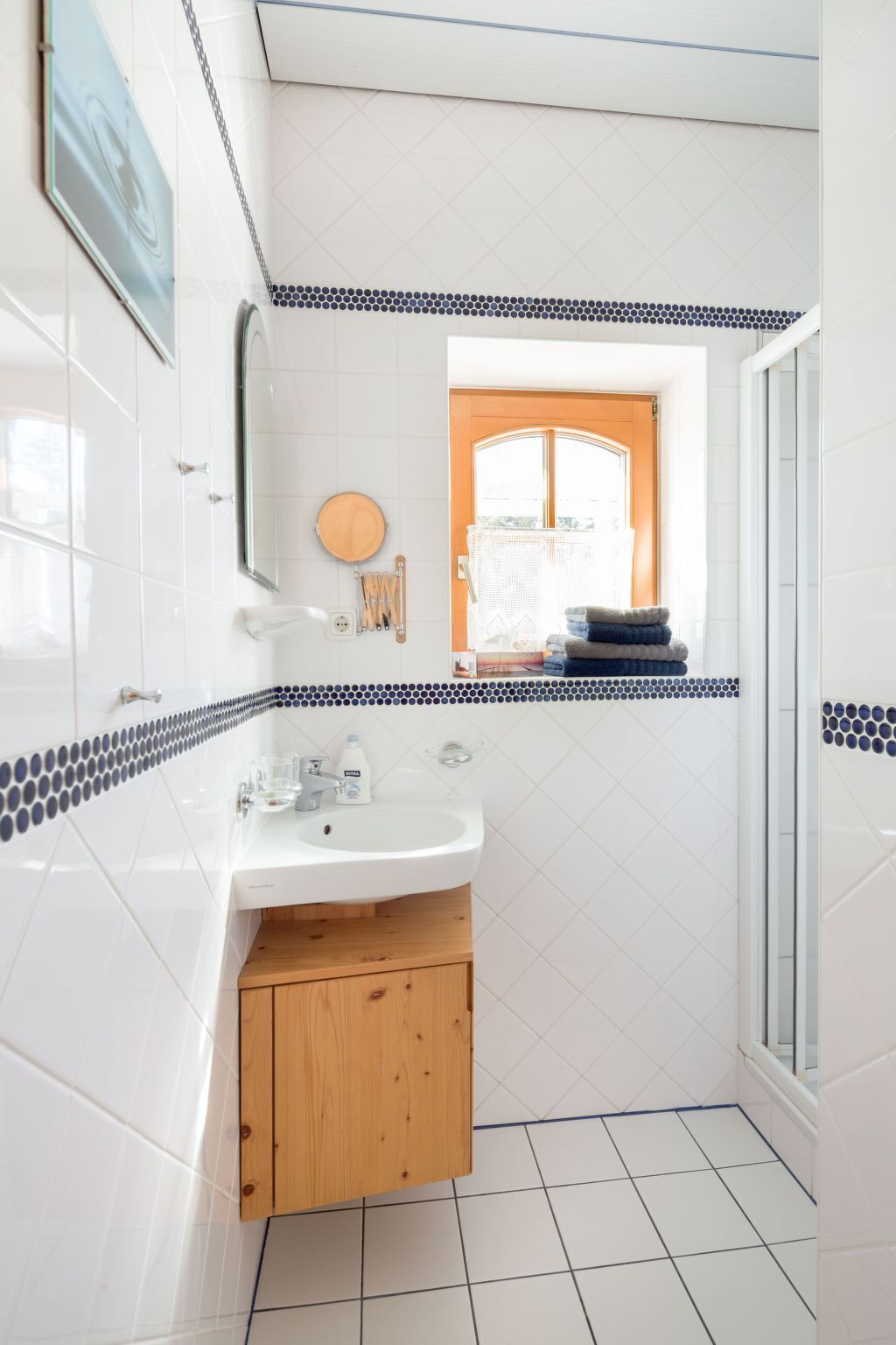 A bathroom with white tiles, a wooden cabinet, a sink, and a window with a view.