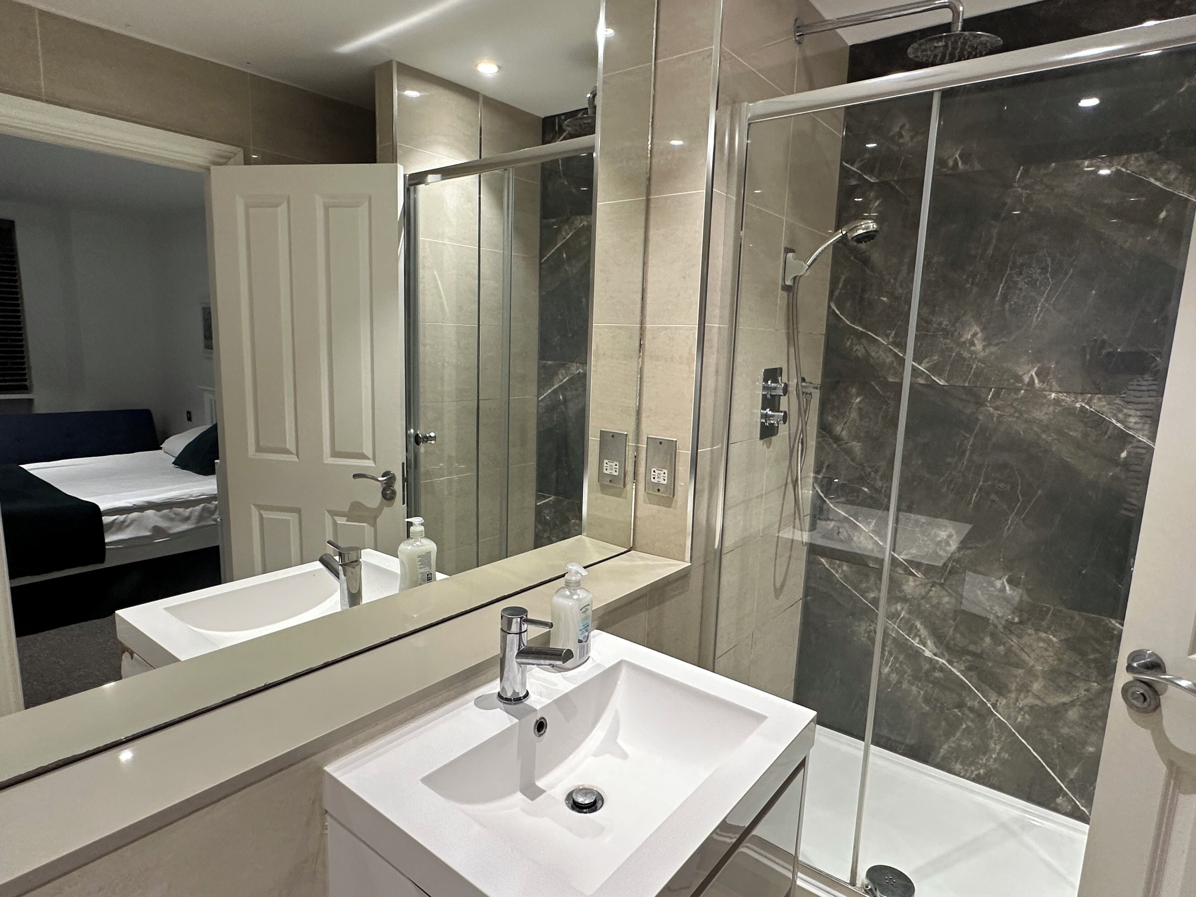 A modern bathroom with a large mirror, a white sink, and a glass-enclosed shower.
