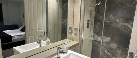 A modern bathroom with a large mirror, a white sink, and a glass-enclosed shower.