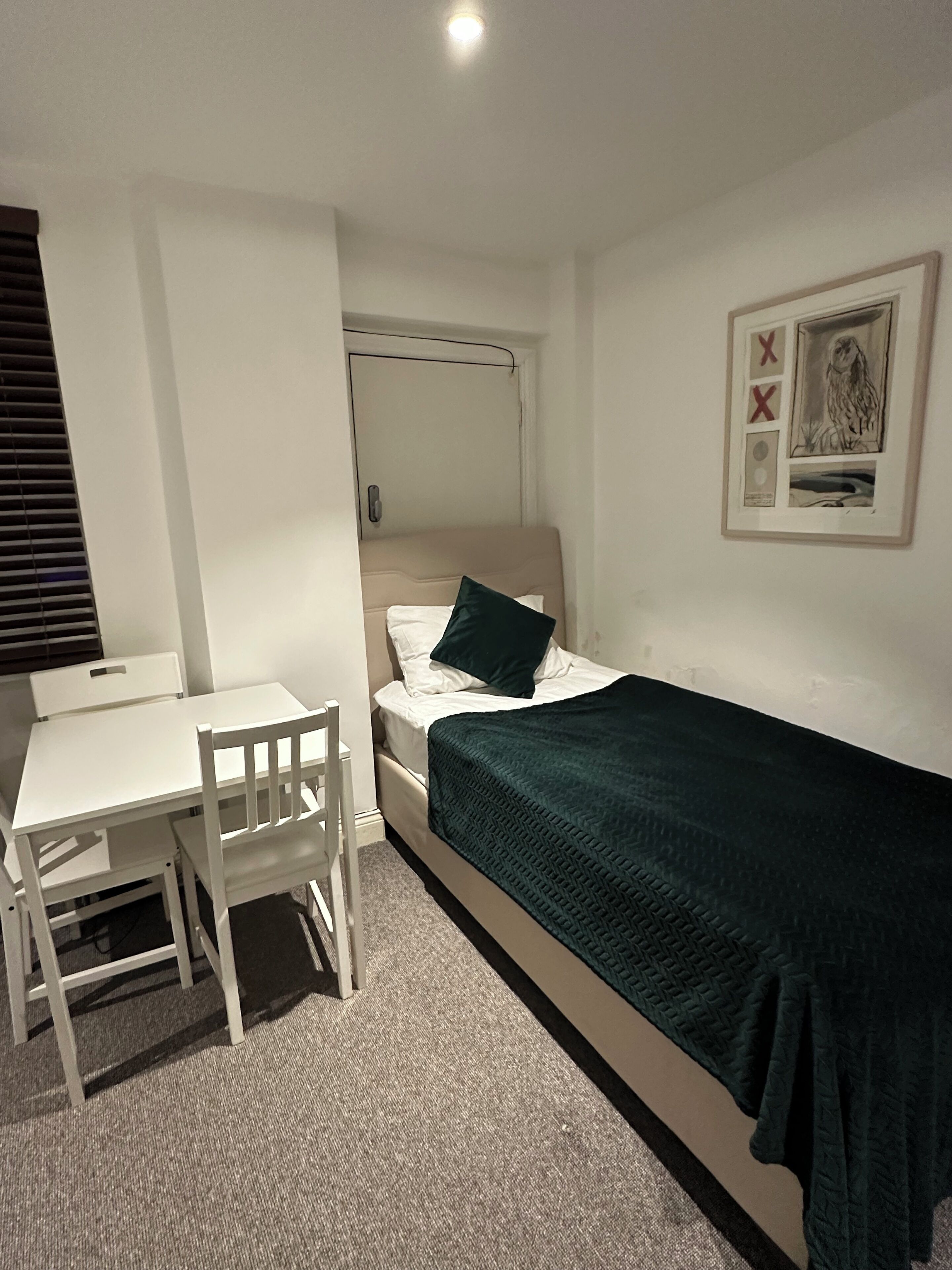 A small, neatly arranged room with a single bed, a bedside table, a chair, and a desk.