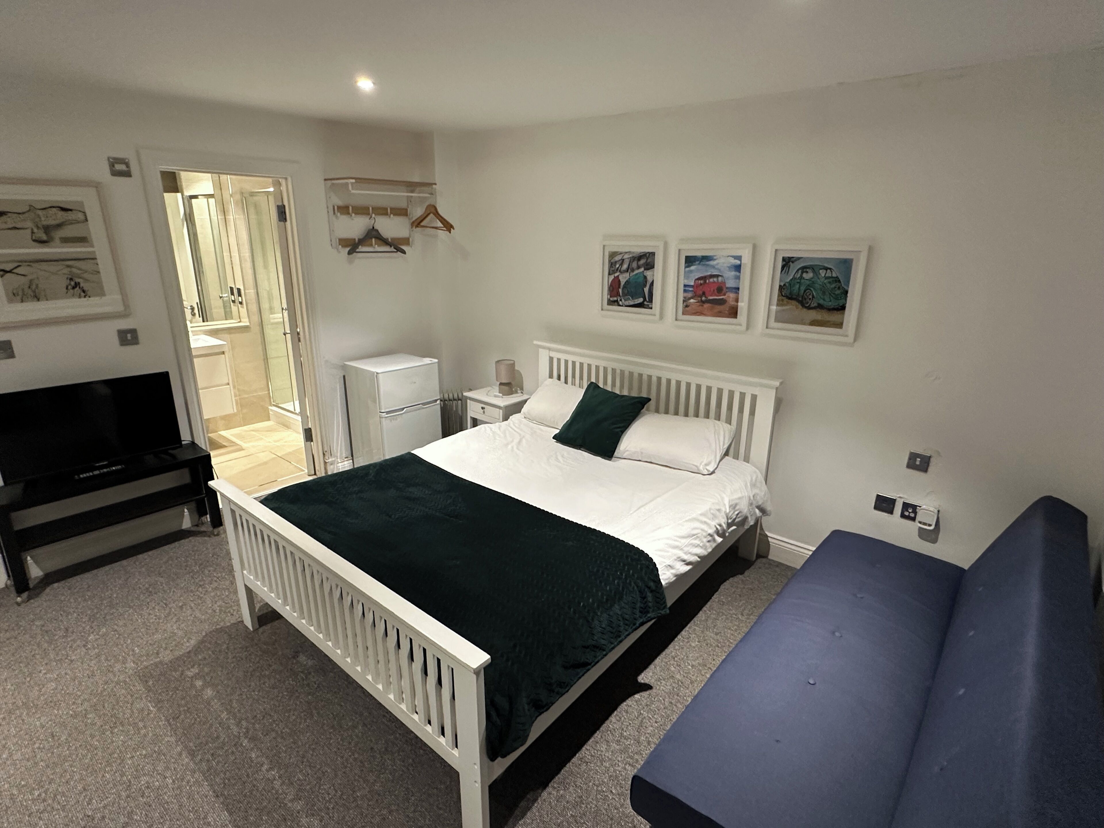 A bedroom with a bed, a TV, a bench, a dresser, and a radiator.